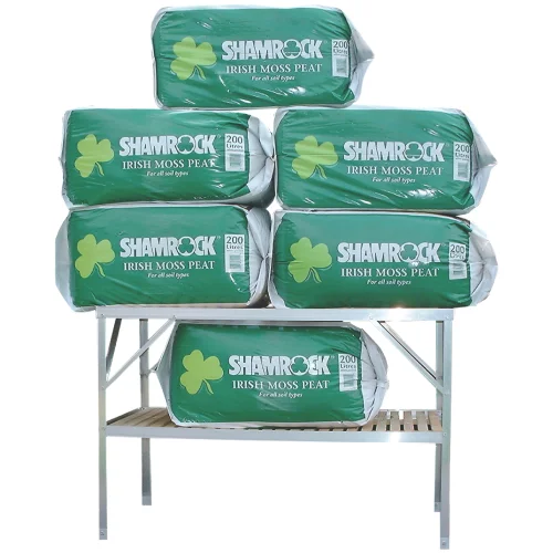 Bags of Shamrock Irish Moss Peat, featuring shamrock symbols and For all soil types, are stacked on a wooden bench. Each bag is labeled 200 Litre in a clear plastic wrapping.