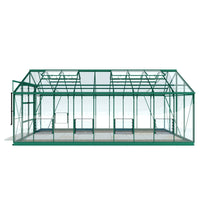 A green Rhino Greenhouse structure stands empty, featuring glass panels and a pitched roof. It is supported by a green metal frame, set against a plain white background.