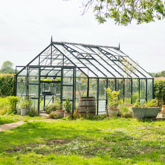 Large 12x16 Rhino greenhouse surrounded by planted pots with a wooden barrel in the foreground