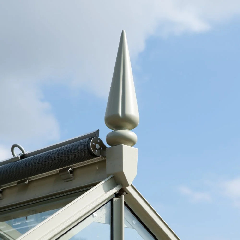 A decorative finial adorns the peak of a Rhino Greenhouse roof, surrounded by clear blue sky, enhancing the structure's elegance and style.