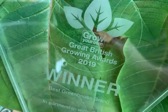 A glass award displays the text: Grow Your Own Great British Growing Awards 2019 WINNER Best Rhino Greenhouse Brand In partnership with... against a backdrop of green leaves.