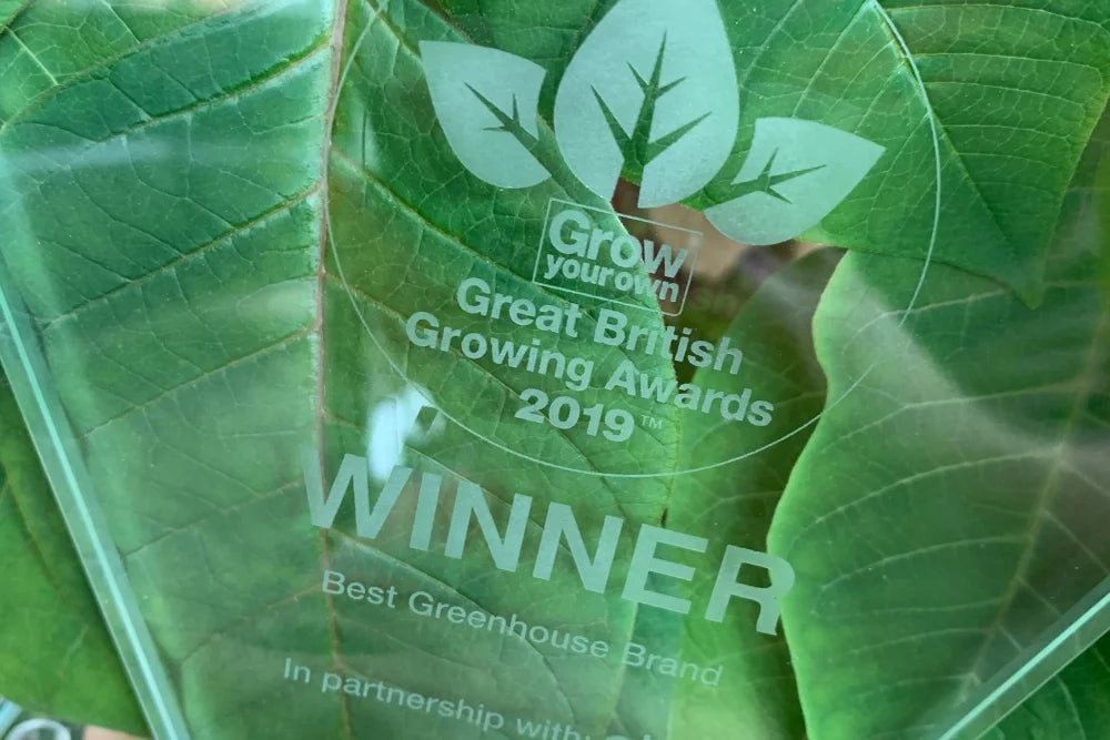 Trophy embossed with leaves and text, Grow your own Great British Growing Awards 2019 WINNER Best Rhino Greenhouse Brand In partnership with. Positioned against a large, textured green leaf background.