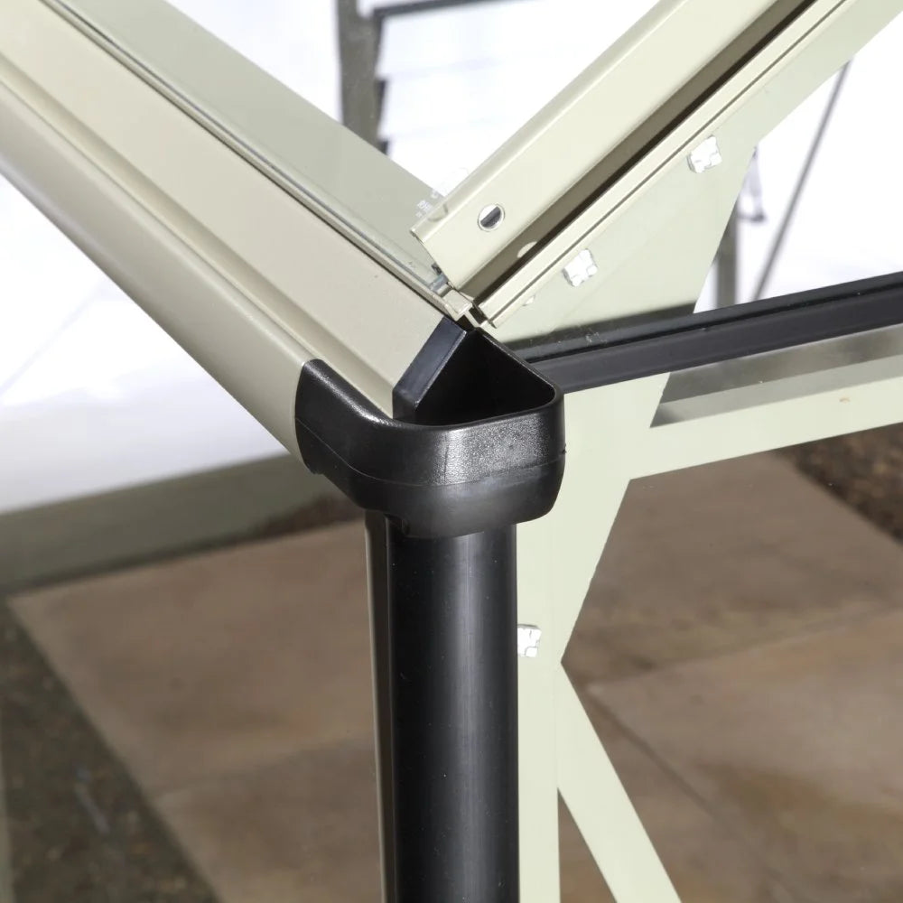 A Rhino Greenhouse corner section with beige aluminum frame and a black plastic connector, set in a garden with tiled flooring, showcasing structural design and material details.