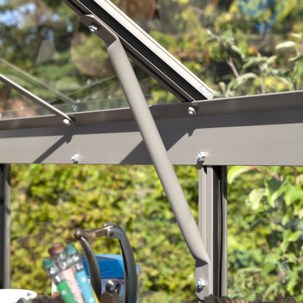 Metal support rod secures Rhino Greenhouse window, surrounded by gardening tools in a sunlit, leafy environment.