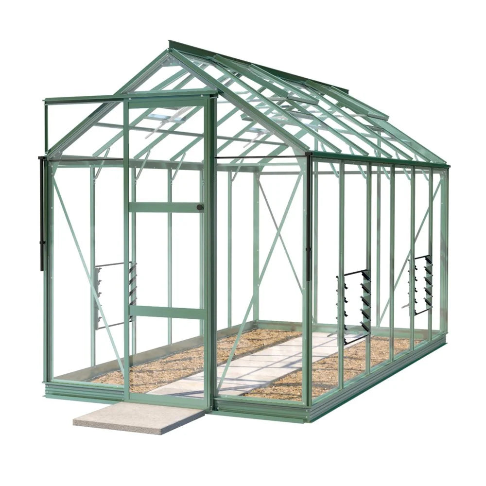A green, rectangular Rhino Greenhouse with a pitched roof and sliding door stands on a gravel pathway, featuring metal framework and transparent panes for optimal light entry.