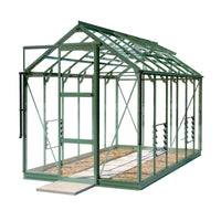 A green metal-framed Rhino Greenhouse stands on a white background, showcasing its transparent panels and front opening door, with a gravel interior and concrete step outside.