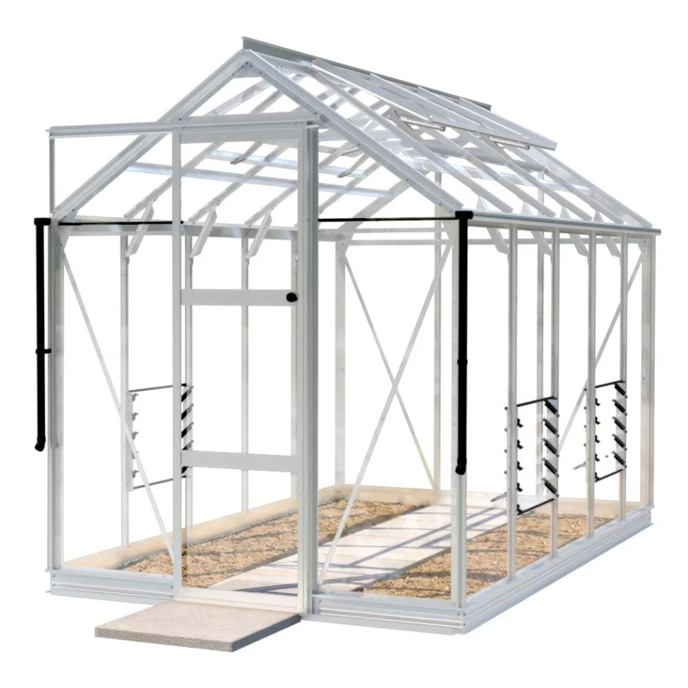 A white-framed Rhino Greenhouse with a hinged door stands on a stone pathway, featuring vented sides and a transparent roof in a spacious outdoor setting.