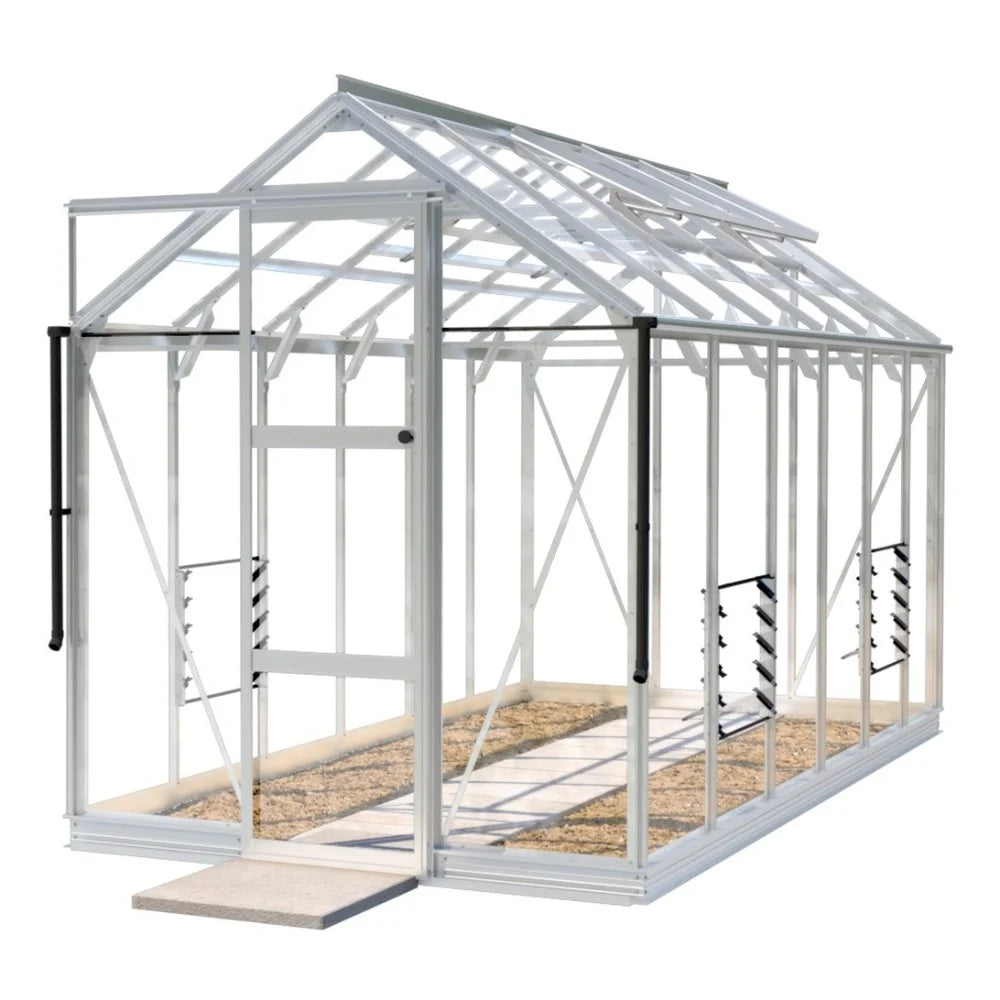 A white-frame Rhino Greenhouse stands with a glass structure, featuring a sliding door and interior shelving, positioned on a concrete base with gravel pathway inside.
