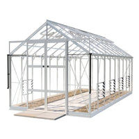 A large, white-framed Rhino Greenhouse with transparent panels stands on a concrete base. It features sliding doors and interior staging shelves, set in a minimalistic outdoor environment.