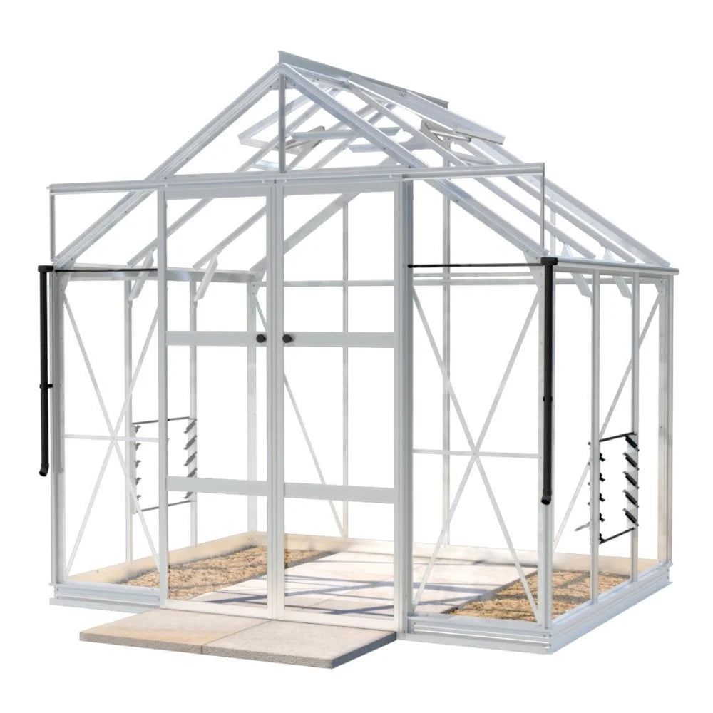 A white-framed Rhino Greenhouse stands with open double doors, showcasing clear panels and roof vents, positioned on a stone-tiled base in a simple, isolated setting.