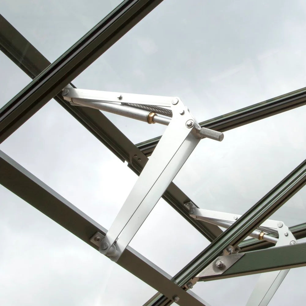 A metal hinge mechanism, designed to open or support a glass panel, is part of a Rhino Greenhouse roof structure, set against a cloudy sky background.