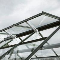 Glass Rhino Greenhouse roof with vent panels slightly open, supported by metal arms; set against a cloudy sky.