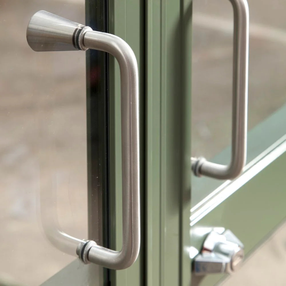 Silver metal handles are fixed on glass doors, with one handle attached to each door. The doors are set within a green metal frame, suggesting an entrance or exit.