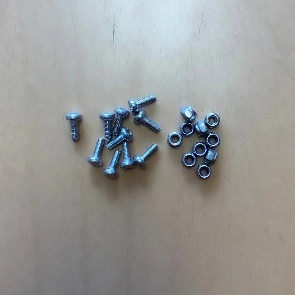 Metal bolts and nuts lie stationary on a light wooden surface, organized in two separate clusters, suggesting preparation for assembly or repair.