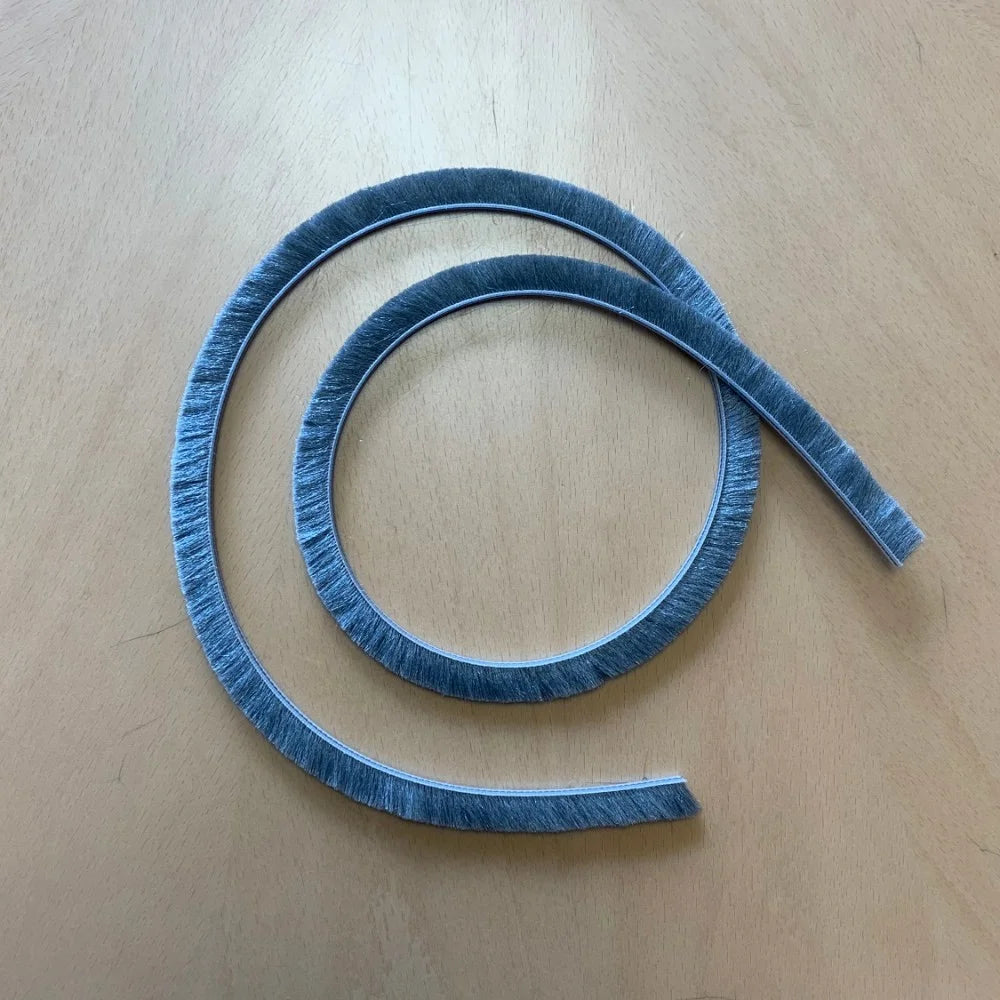 A coiled strip of gray bristle material rests on a wooden surface, forming a spiral shape.