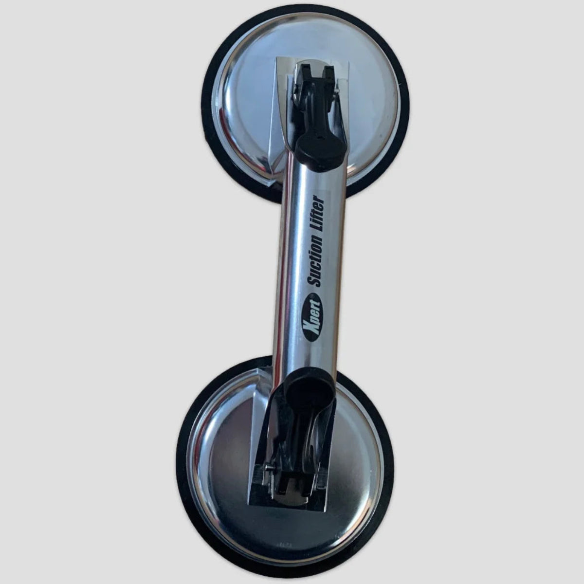 A metallic dual suction lifter, labeled Xpert Suction Lifter, with two suction cups for lifting objects, displayed against a plain gray background.
