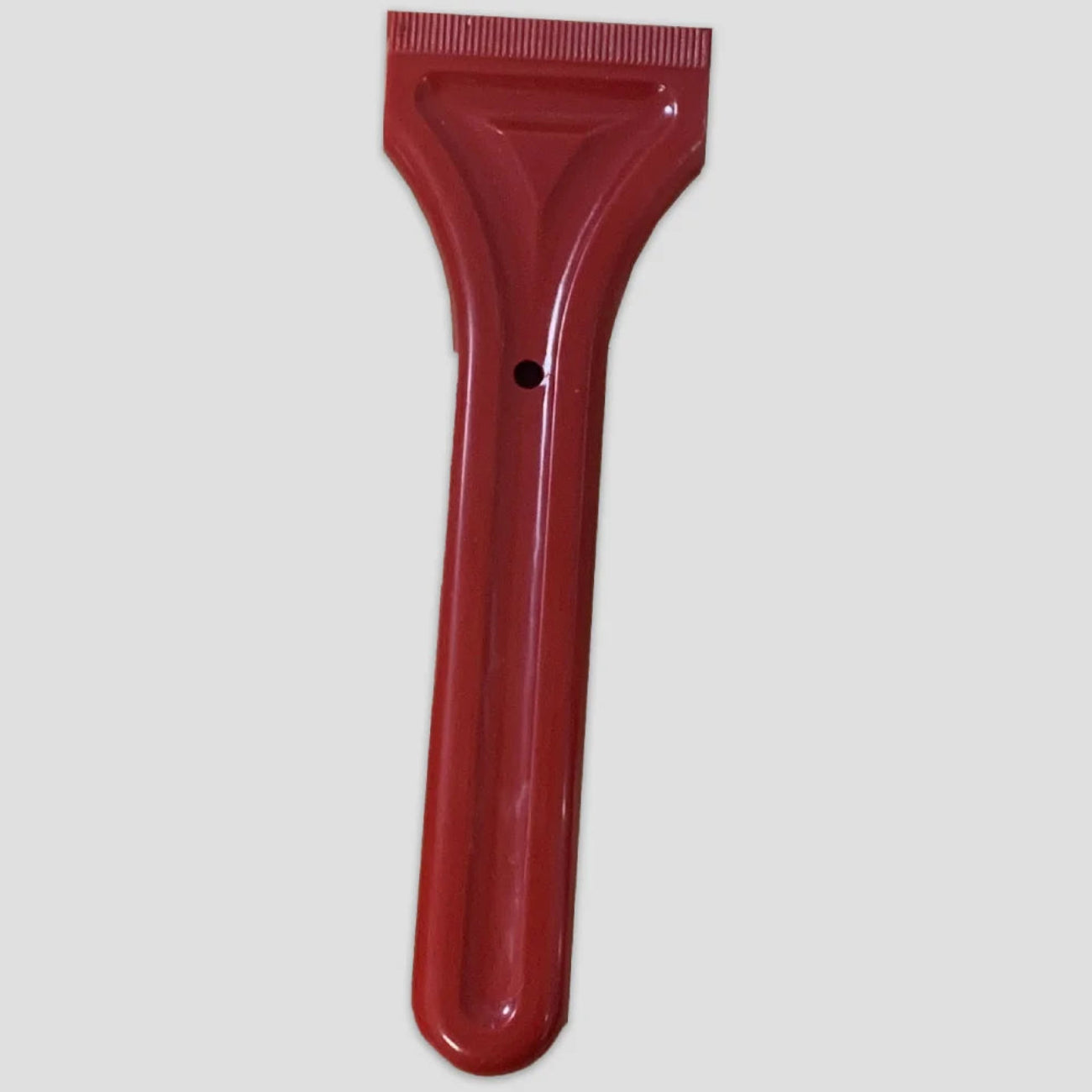 Red plastic scraper with a flat, ridged edge and long handle featuring a hole for hanging; set against a neutral gray background.