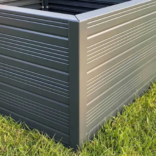 A Rhino metal raised garden bed with horizontal grooves stands firmly on lush green grass, showcasing its metallic design in an outdoor setting.