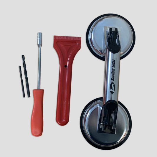 Tools for Rhino Greenhouse installation: two drill bits, a screwdriver, a red scraper, and a metal suction lifter labeled Neta Suction Lifter arranged on a plain surface.