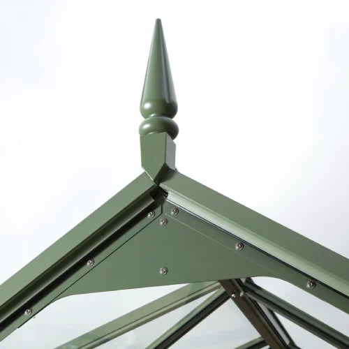 A green metal Rhino Greenhouse roof corner with a decorative finial. The structure features riveted panels and intersecting beams. The background is a plain white, emphasizing the Rhino Greenhouse's design.