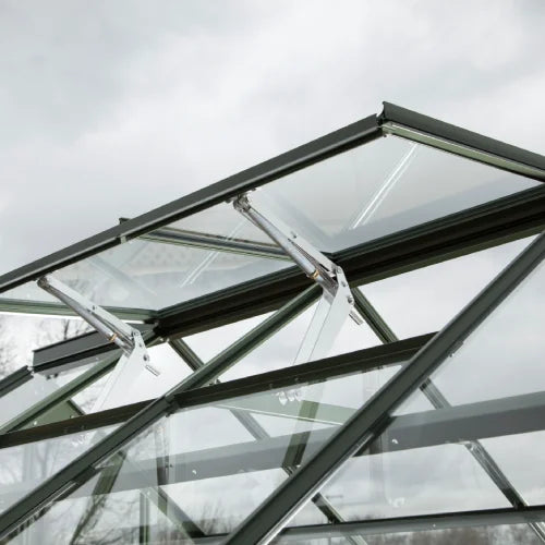 Glass panels are angled upwards as an automatic venting mechanism opens them within a Rhino Greenhouse structure. The sky is overcast in the background, suggesting an outdoor setting.